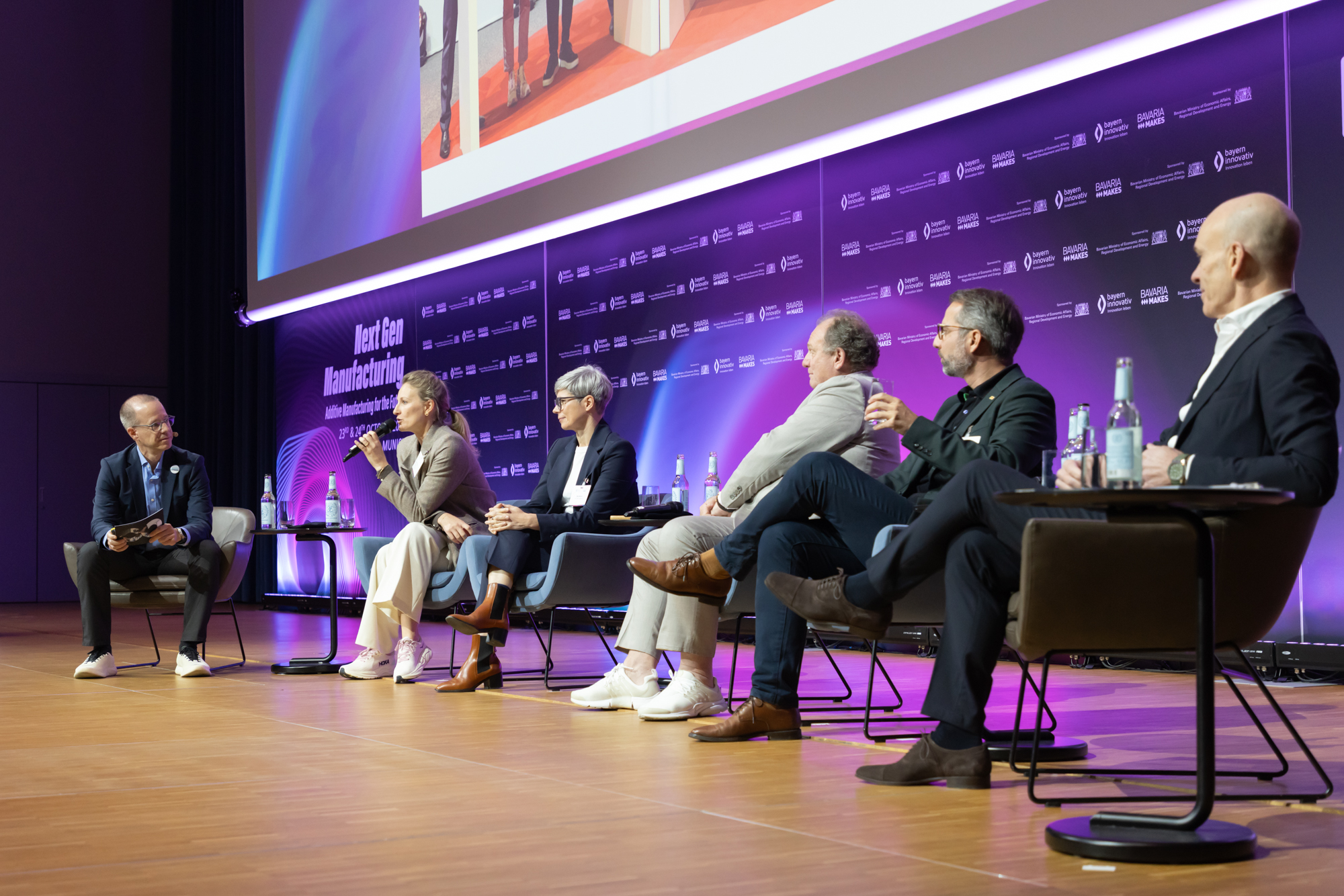 Podiumsdiskussion mit fünf Personen auf der Bühne, lila Hintergrundbeleuchtung. Aufgenommen beim AM Kongress.