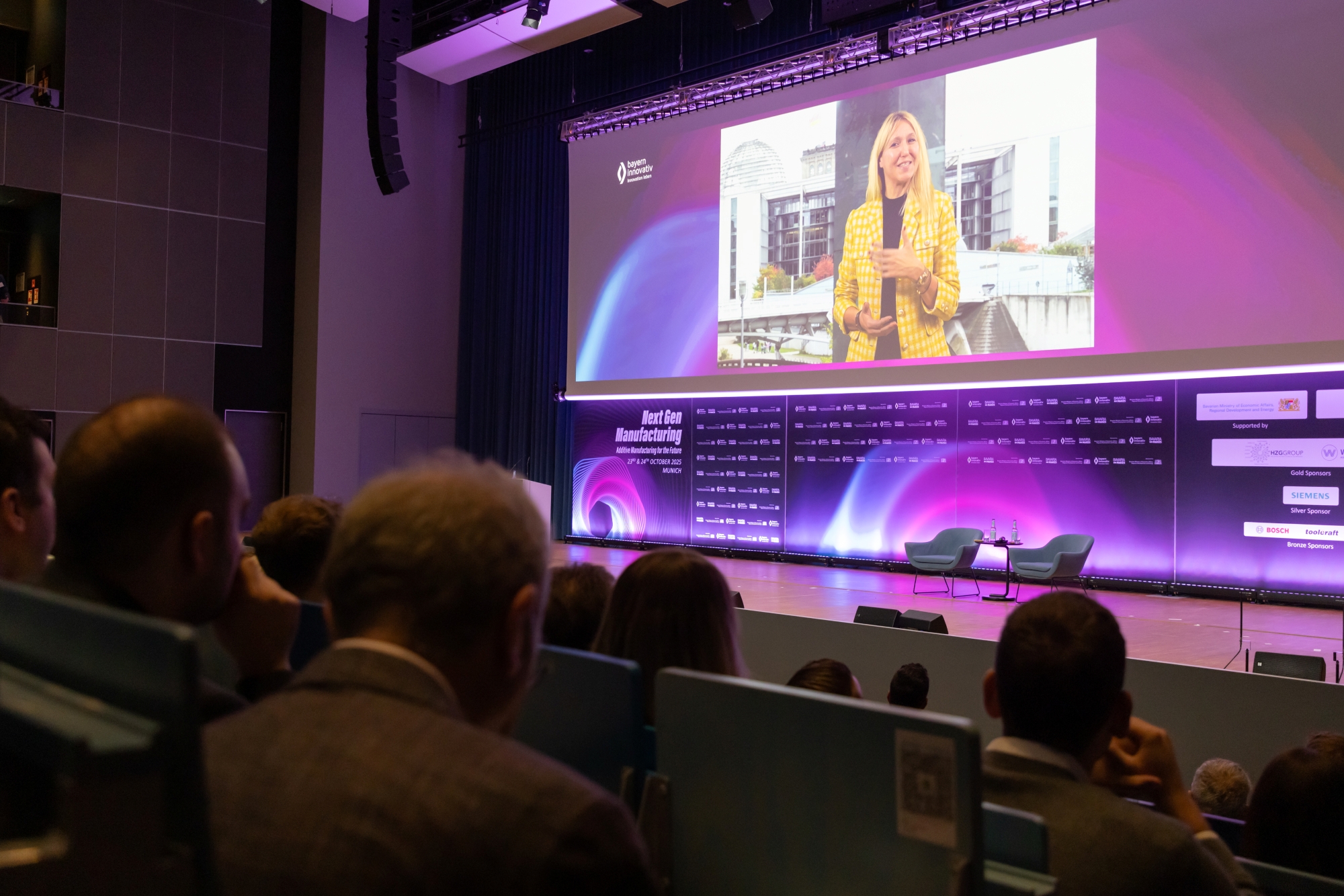 Publikum sitzt in einem Konferenzsaal und verfolgt eine Präsentation auf einer großen Leinwand. Aufgenommen beim AM Kongress.