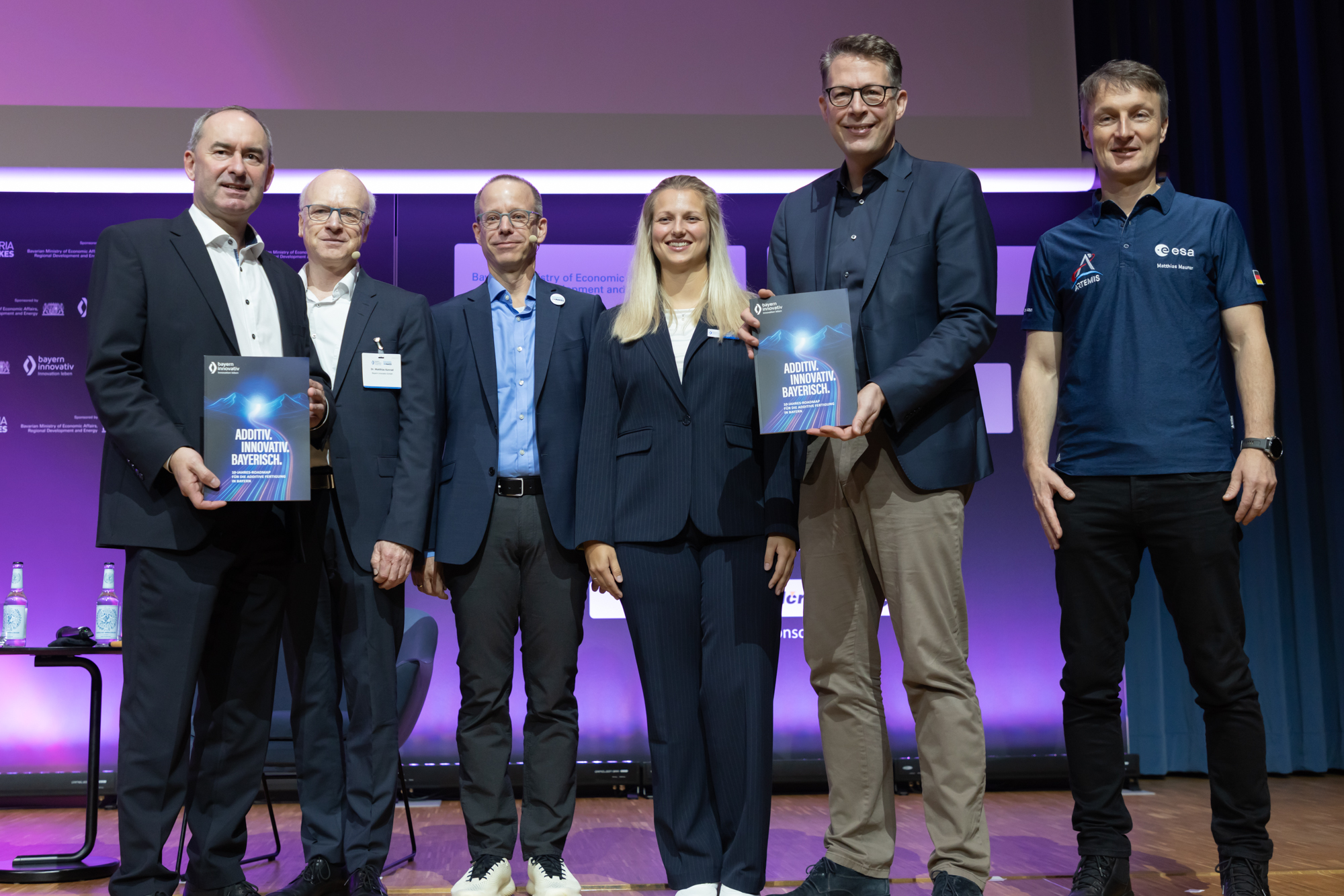 Gruppe von sechs Personen steht auf der Bühne und hält Urkunden oder Auszeichnungen. Aufgenommen beim AM Kongress.