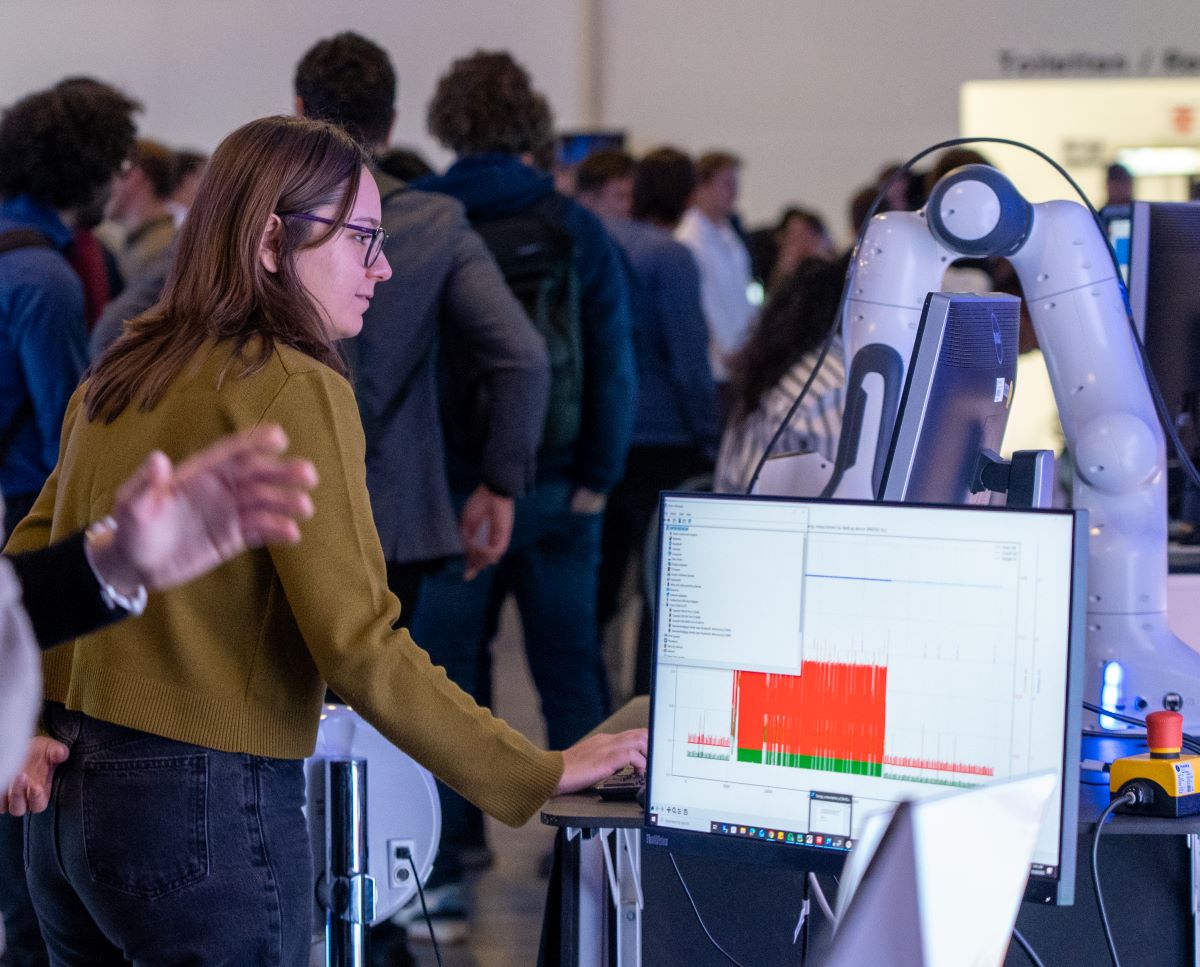 A booth on the Thinknet 6G Summit, with a woman puting data into a PC to steer a robotic arm.