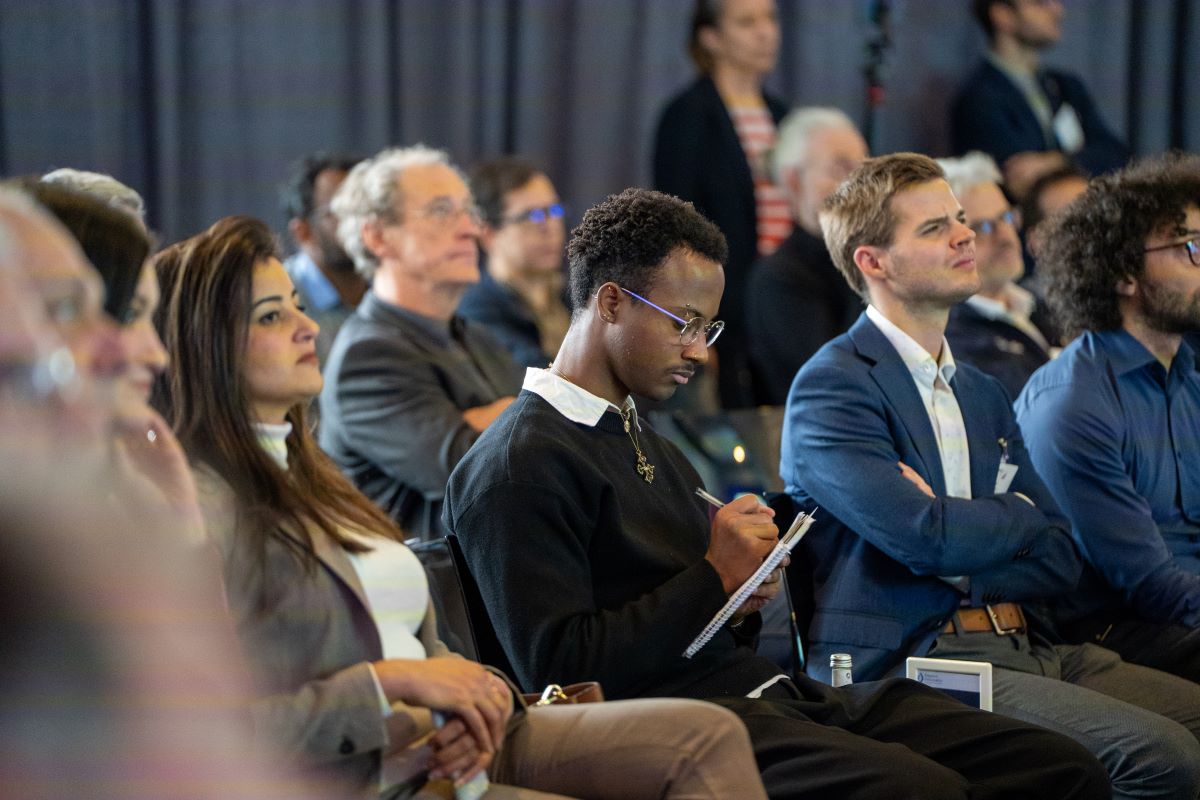 People sitting in front of the Thinknet 6G Summit stage, listening to the speaker and taking notes.