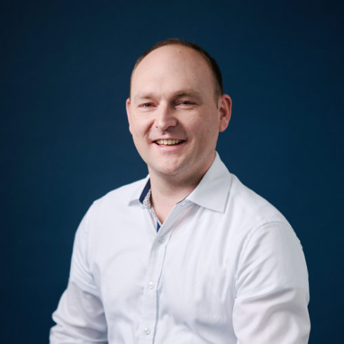 Mann mit Halbglatze in weißem Hemd vor dunkelblauem Hintergrund