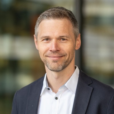 Portraitbild von Prof. Dr. Mirko Mähisch, welches einen Mann in einem weißen Hemd mit schwarzen Sakko, gräulichen Haaren und drei Tage Bart zeigt