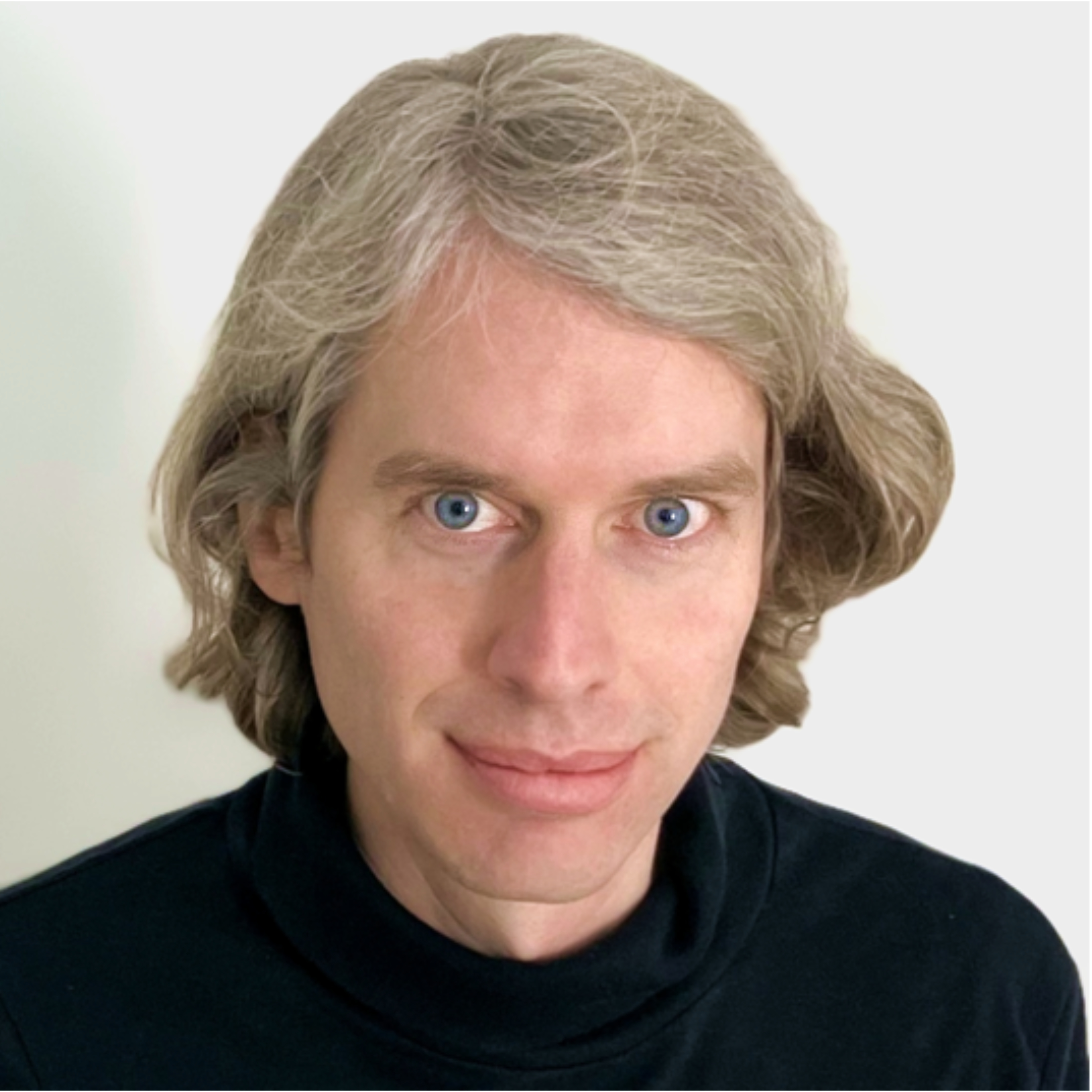 Portraitbild des Referenten Tom Giovanazzi, welches einen Mann mit schwarzem Pulli und schulterlangen grau blonden Haaren vor weißem Hintergrund zeigt.