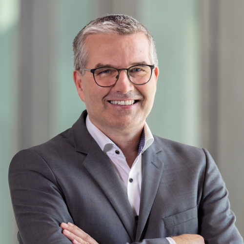 Ein Mann mit Brille und Anzug lächelt freundlich in die Kamera.