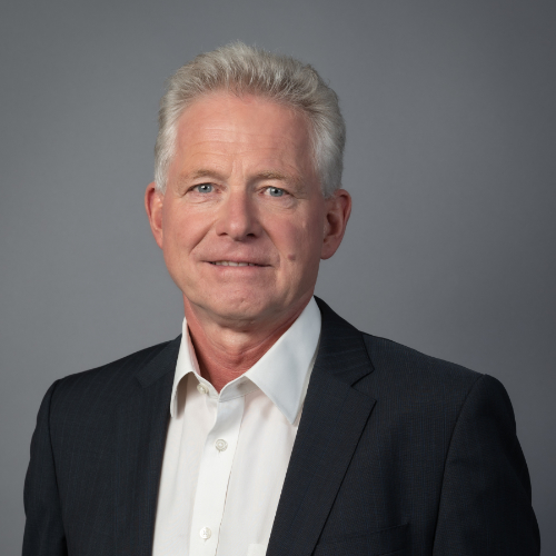 Ein Mann in formeller Kleidung steht vor einer Wand.