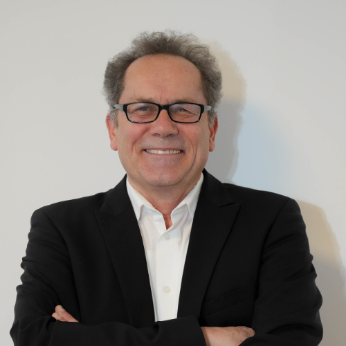 Ein Mann in formeller Kleidung steht vor einer Wand.