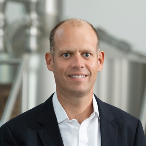 Ein Mann in formeller Kleidung steht vor einem Sudkessel.