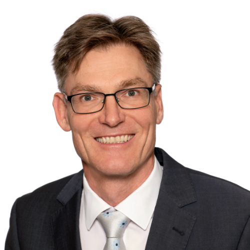 Ein Mann in formeller Kleidung steht vor einer Wand.