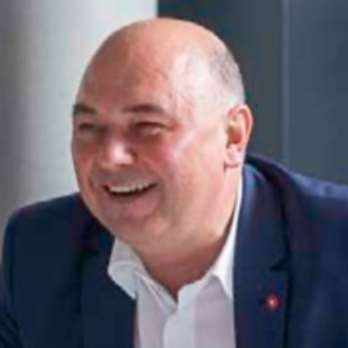 Ein glatzköpfiger Mann in einem Anzug sitzt an einem Tisch.