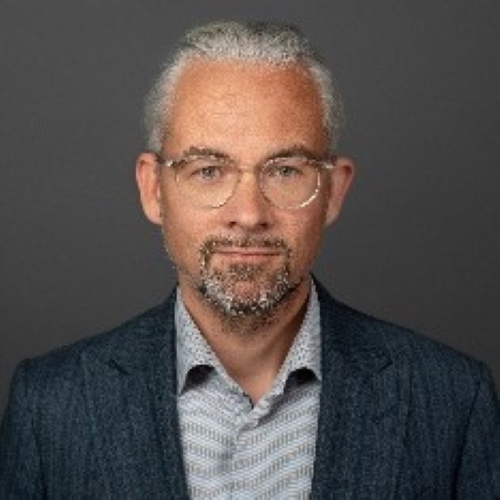 Ein Mann in einem Anzugjackett und mit Brille schaut in die Kamera.