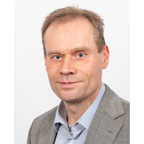 Ein Mann in formeller Kleidung steht vor einer Wand.