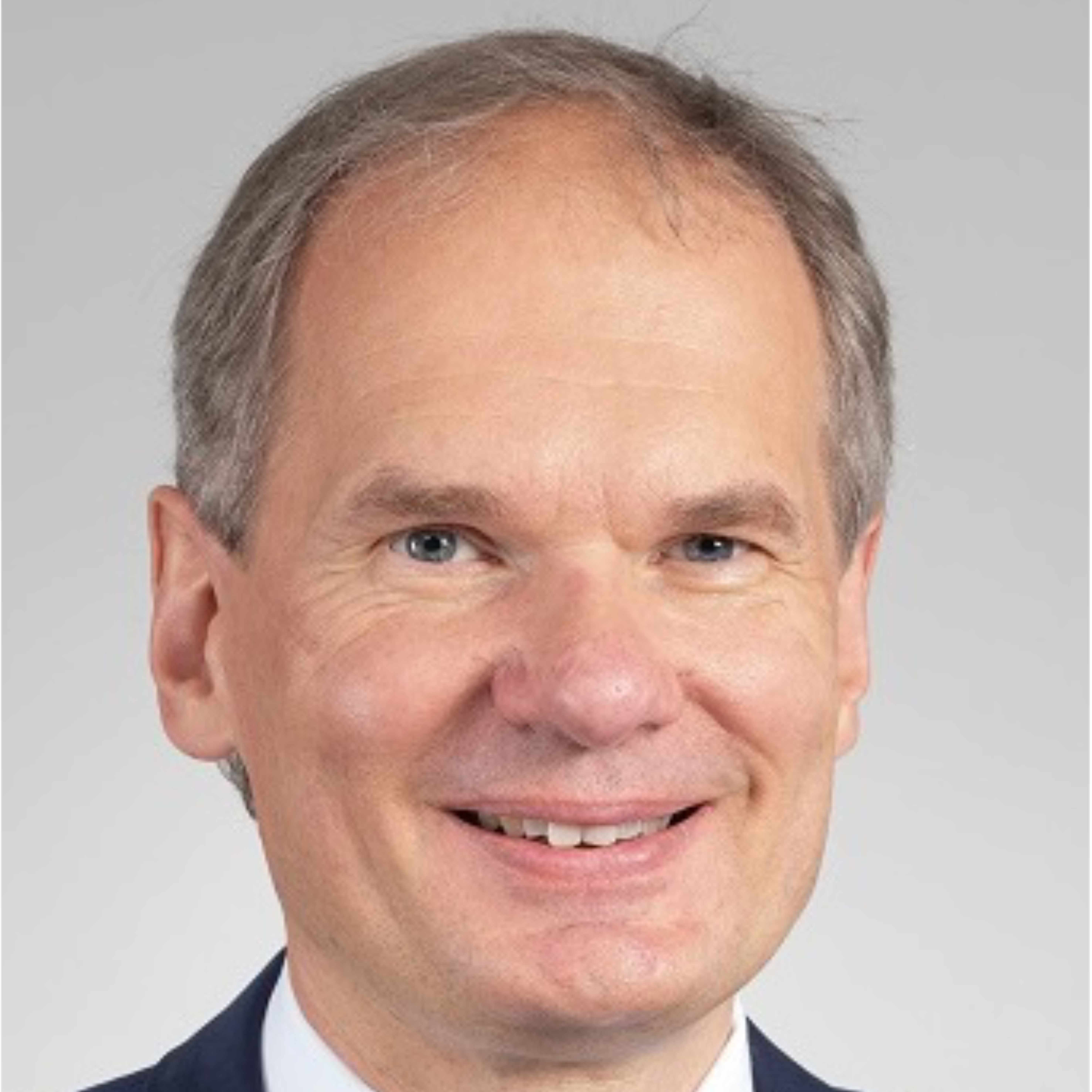 Ein grauhaariger Mann trägt einen Anzug und lächelt in die Kamera.