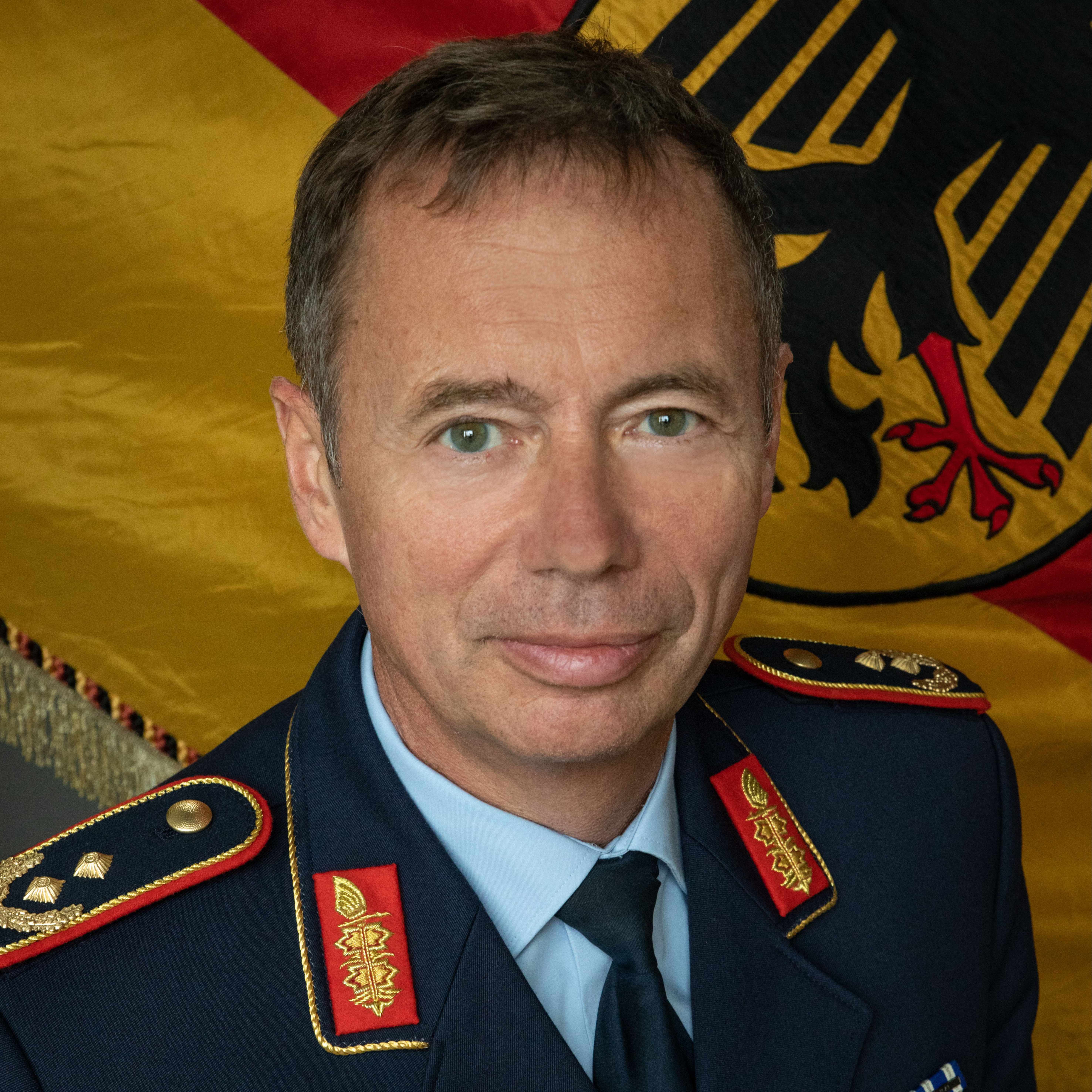 Ein Mann in militärischer Uniform vor einer deutschen Flagge.