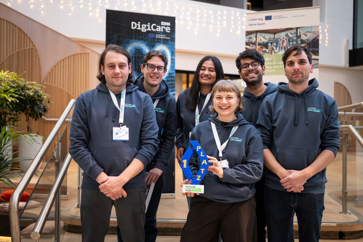 „Teilnehmer eines Hackathons arbeiten gemeinsam an Laptops in einem modernen Raum, umgeben von Bannern und Präsentationsmaterial.“