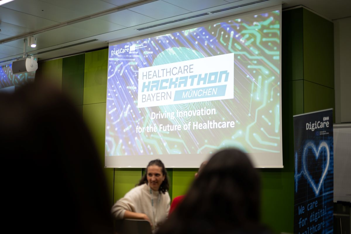 Eine Frau ist vor einer Leinwand mit einem Hackathon Logo zu sehen