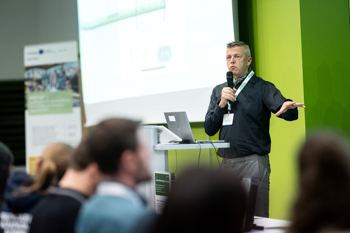 Ein Mann hält einen Vortrag, eine große Leinwand ist zu sehen