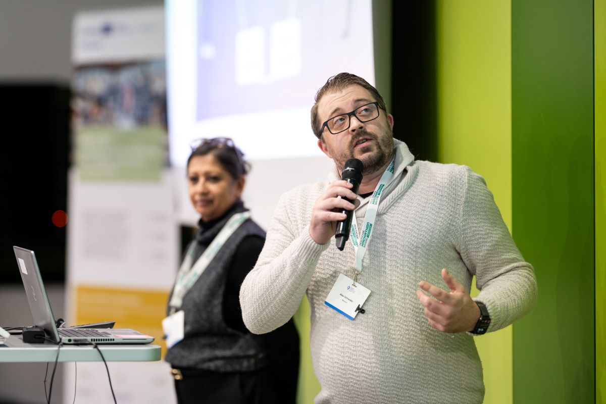 Ein Mann und eine Frau halten einen Vortrag und stehen vor einem grünen Hintergrund