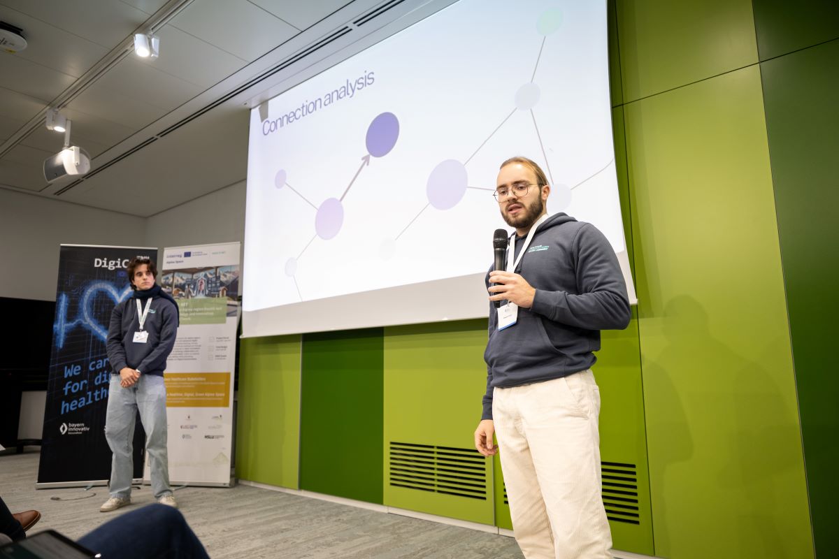 Auf dem Bild sind zwei Männer zu sehen, welcher vor einer Leinwand stehen und einen Vortrag halten.