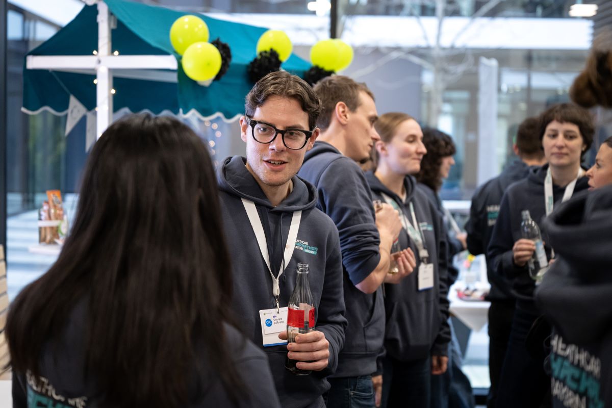 Das Bild zeigt eine Gruppe von Menschen, die wahrscheinlich an einem Event oder einer Konferenz teilnehmen. Die meisten tragen passende Kapuzenpullover mit einem Logo und Namensschilder.