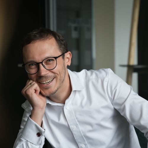 Auf dem Bild ist ein Herr mit weißem Hemd und schwarzer Brille zu sehen