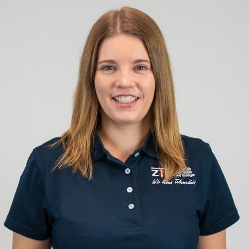 Frau mit schulterlangem, glattem Haar trägt ein dunkelblaues Poloshirt mit dem Logo und Schriftzug "ZTM Bayern" auf der linken Brustseite