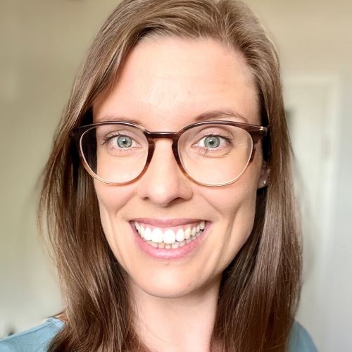 Frau mit schulterlangem, glattem, braunem Haar und silbernen Ohrringen vor hellem Hintergrund