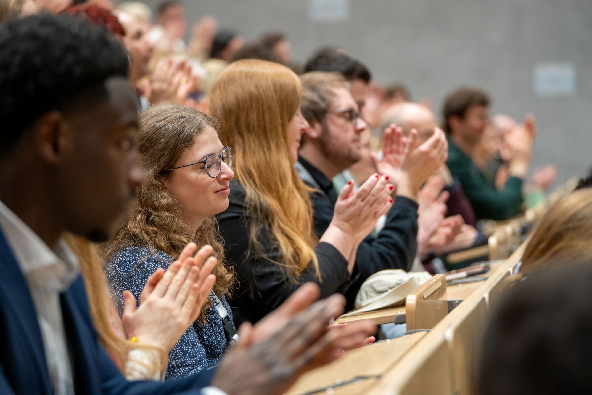 Menschen sitzen in einem Hörsaal und klatschen applaudierend