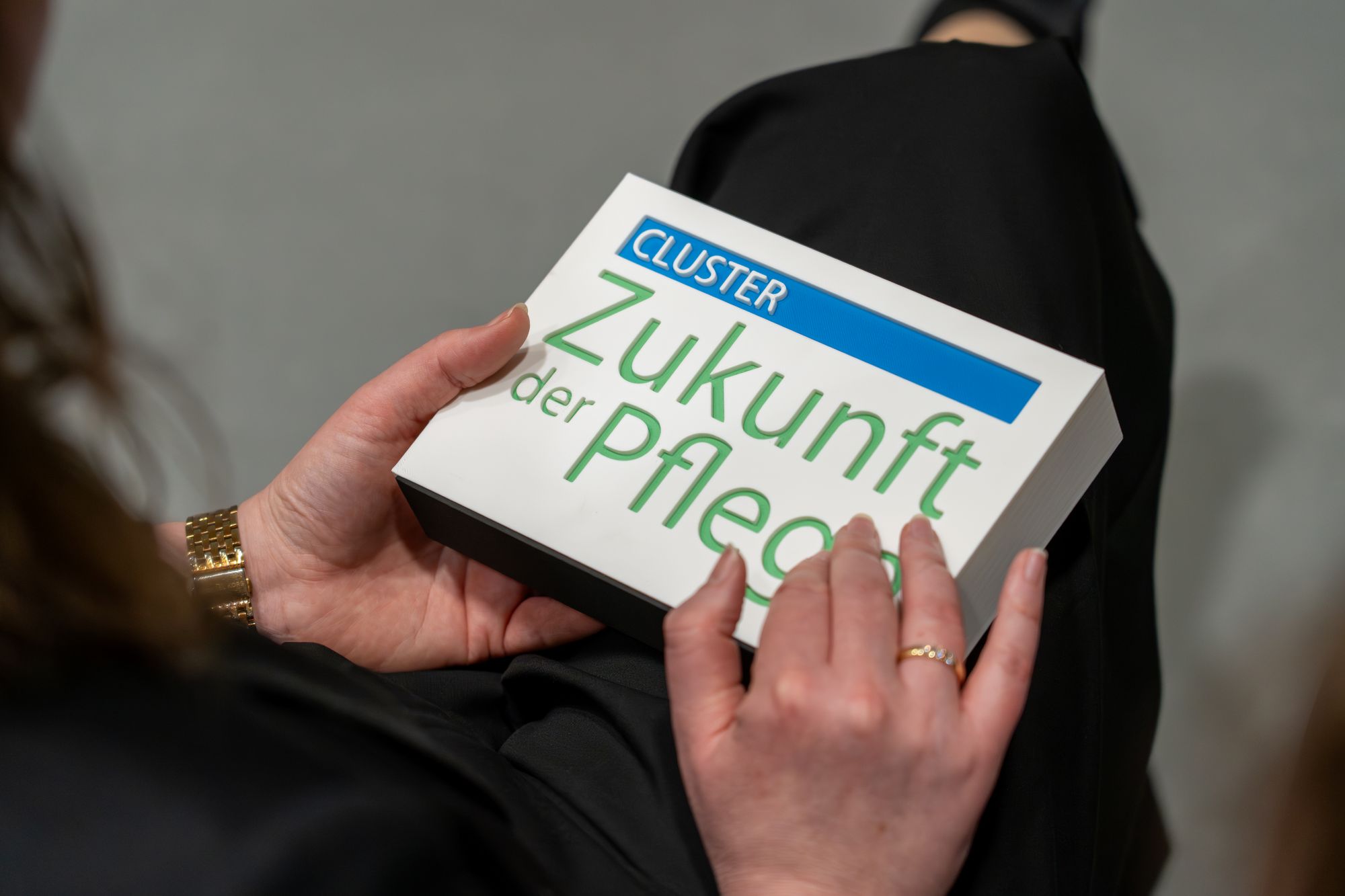 Hände halten eine Karte mit dem Text 'CLUSTER Zukunft der Pflege'