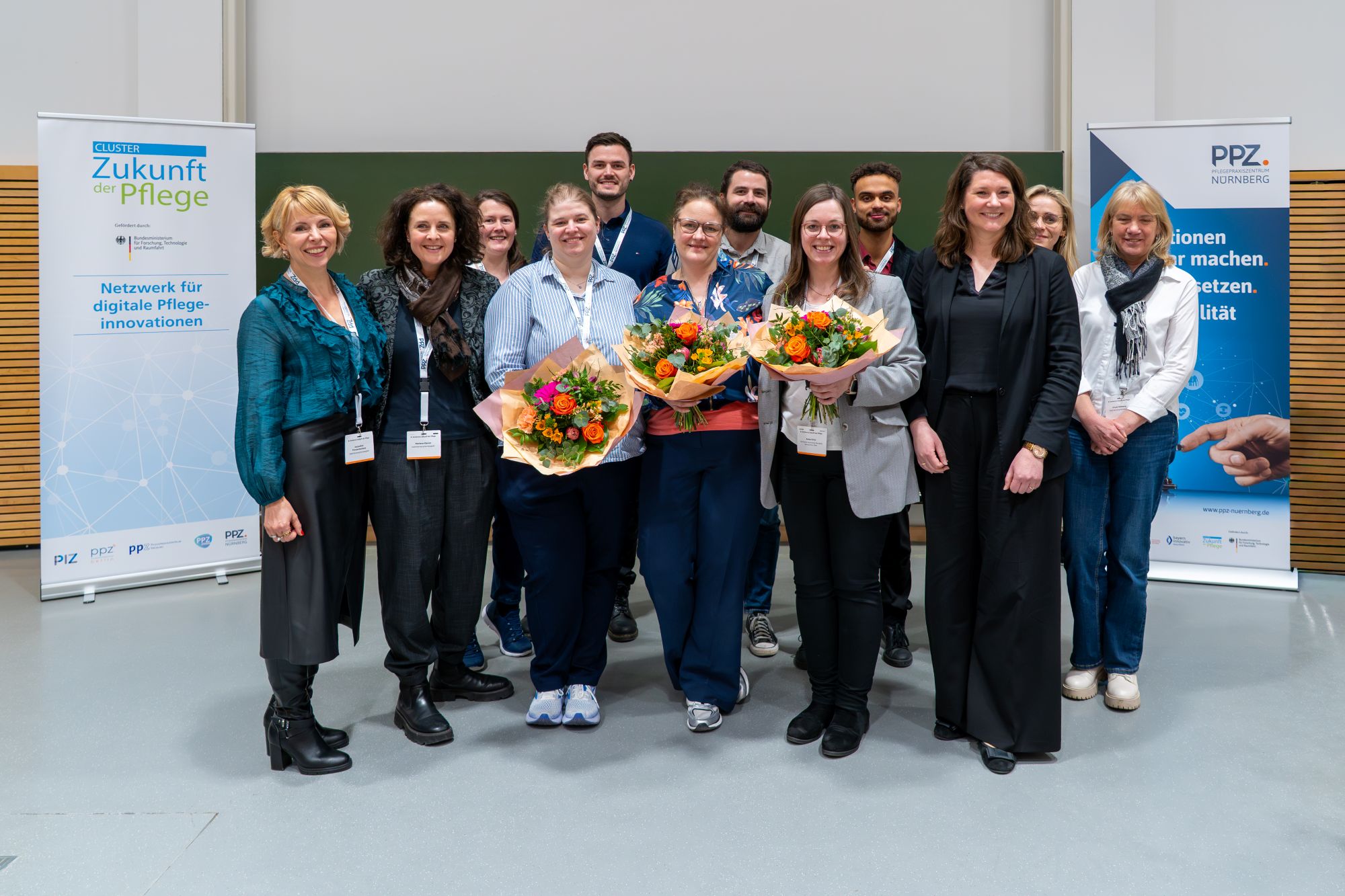 Gruppe von Menschen steht vor zwei aufrechten Bannern mit Texten zu Pflegeinnovationen und PPZ Nürnberg, drei Personen halten Blumensträuße