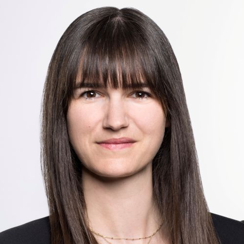 Person mit glattem, schulterlangem Haar und dunkler Kleidung vor hellem Hintergrund.