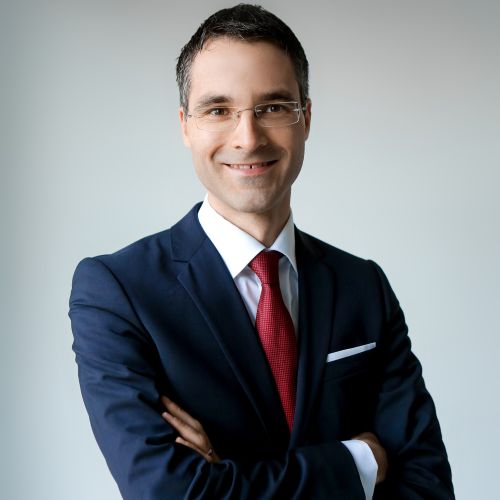 auf dem Bild ist ein Herr in Anzug und roter Krawatte zu sehen.