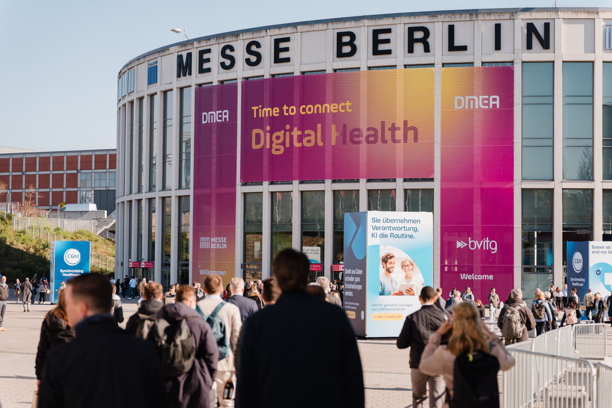 Menschenmenge vor dem runden Eingangsgebäude der Messe Berlin mit großen Bannern zur DMEA Digital Health
