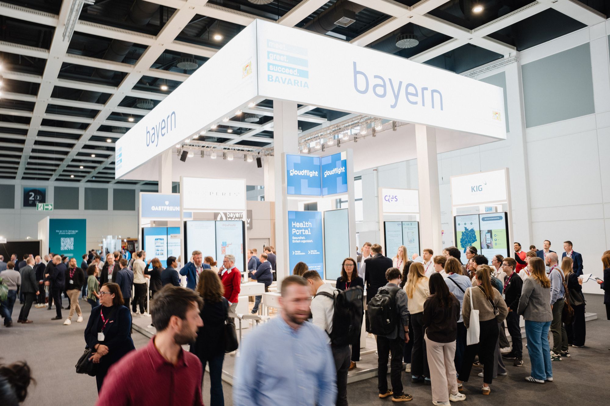 Messestand mit der Aufschrift »bayern« auf einem großen weißen Banner über einem belebten Ausstellungsbereich mit vielen Menschen in einer Halle