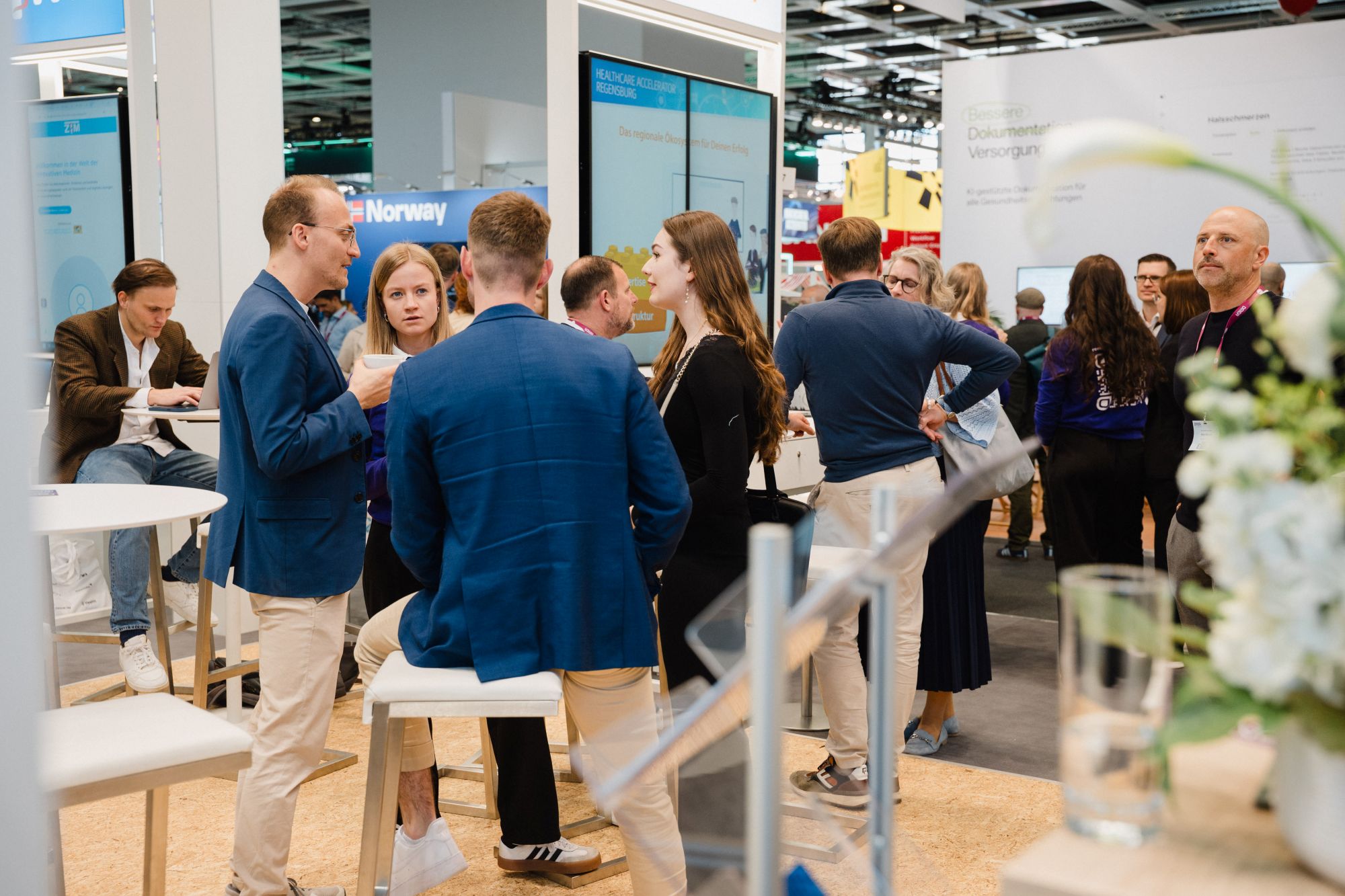Mehrere Personen stehen und sitzen in einem hellen, modernen Messestandbereich und unterhalten sich