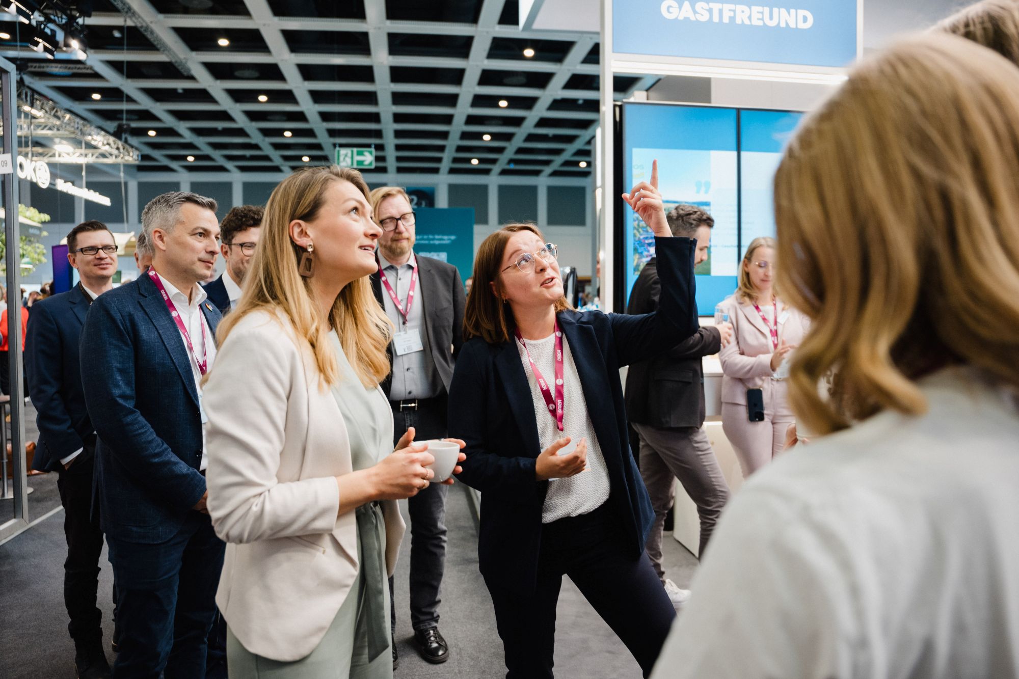 Gruppe von Menschen mit Namensschildern in einem modernen Innenraum, eine Frau zeigt mit dem Finger nach oben
