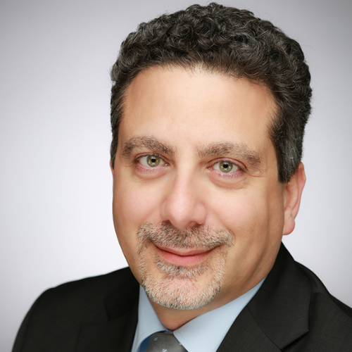 Portraitbild von Mann mit grauen Bart und dunklen Haaren, schwarzes Sakko und hellblaues Hemd