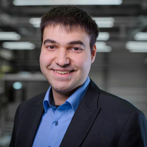 Mann mit schwarzen kürzeren Haaren, blauem Hemd und schwarzem Anzug