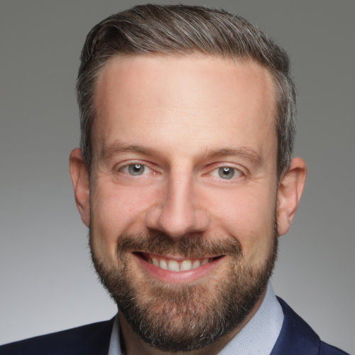 Portraitbild eines Malles mit Bart der in die Kamera lächelt