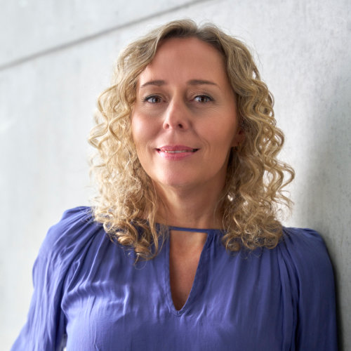 Bild einer blonden Frau mit Locken in einer lilafarbenen Bluse