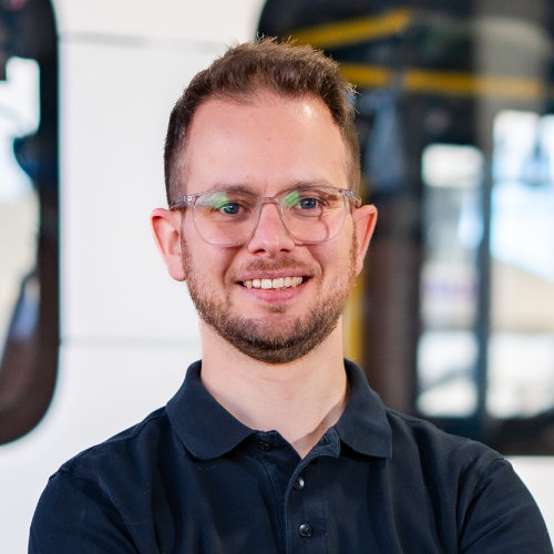 Das Bild zeigt einen lächelnden Mann mit Brille, Bart und einem schwarzen Poloshirt