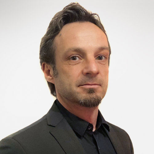 Das Bild zeigt einen Mann in schwarzen Hemd mit dunkelgrauem Sakko und einem Bart