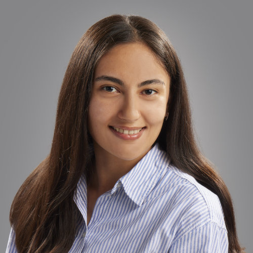 Portraitbild von Olima Negmatova, einer Frau  mit braunen, langen Haaren und einer hellblau und weiß gestrieften Bluse