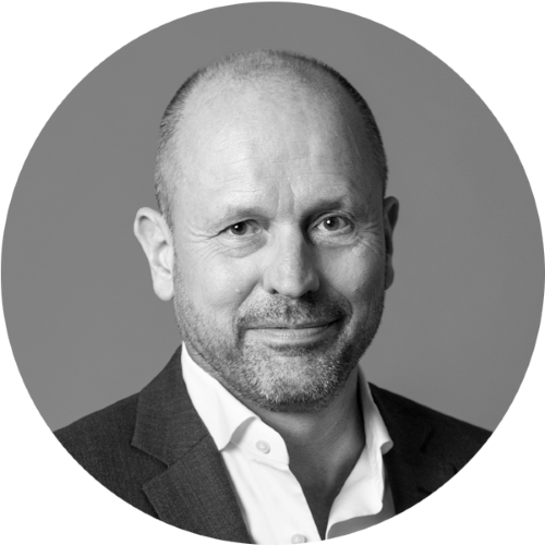 Mann mit kurzem Haar trägt weißen Hemdkragen und dunkles Sakko vor einfarbigem Hintergrund