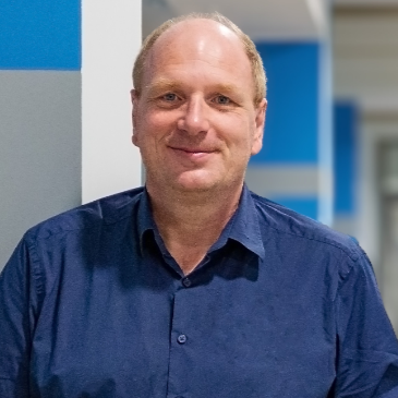 Mann mit blauem Hemd vor blau-weißer Wand