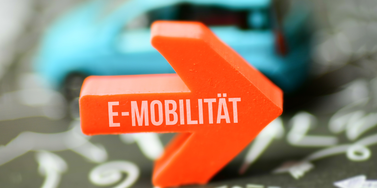 Zu sehen ist ein oranger Rechtspfeil, auf dem E-Mobilität steht mit einem kleinen blauen Auto im Hintergrund.