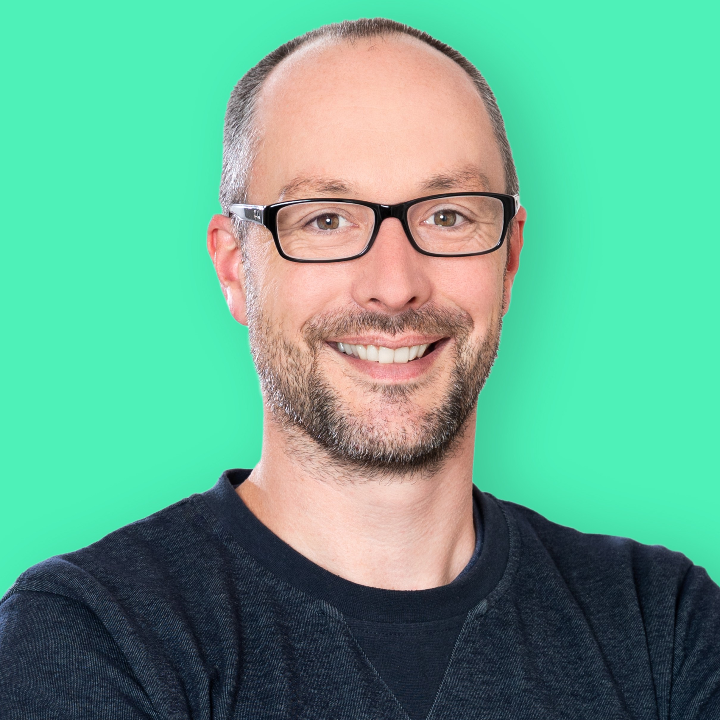 Oberkörperaufnahme eines Mannes mit Brille und dunklem Pullover vor grünem Hintergrund