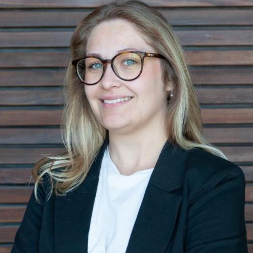 Blonde Frau mit weißem Hemd und schwarzen Blaser und im Hintergrund eine Sprossenwand