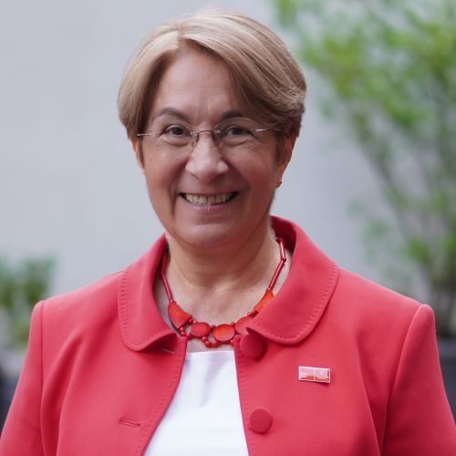 auf dem Bild ist eine Frau mit rotem Blazer und weißem Tshirt zu sehen.