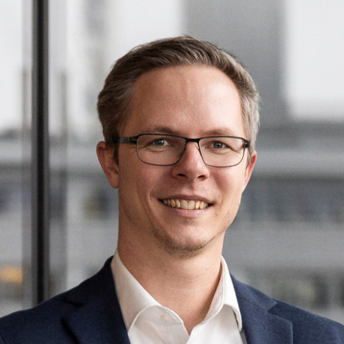Ein Mann mit Brille und Anzug lächelt freundlich in die Kamera.